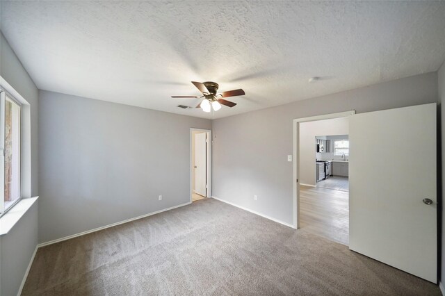 empty room featuring ceiling fan, a textured ceiling, and light carpet