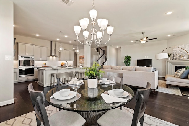 dining space with sink, dark wood-type flooring, and ceiling fan with notable chandelier