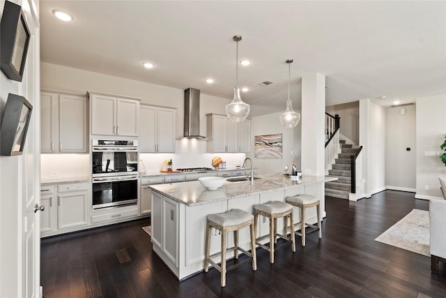 kitchen with white cabinets, wall chimney exhaust hood, sink, and hanging light fixtures