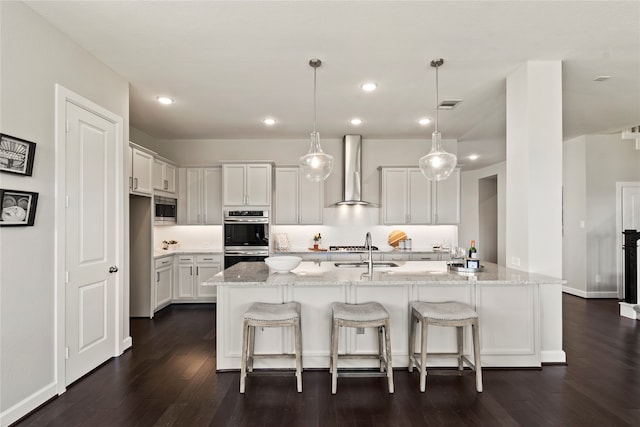 kitchen with appliances with stainless steel finishes, dark hardwood / wood-style flooring, wall chimney range hood, decorative light fixtures, and white cabinets