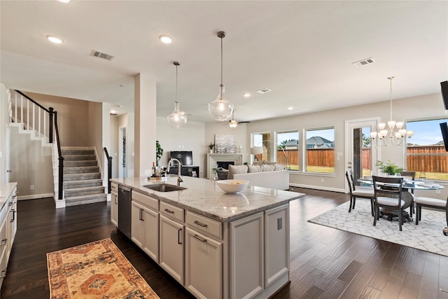 kitchen featuring sink, light stone counters, dark hardwood / wood-style flooring, stainless steel dishwasher, and an island with sink