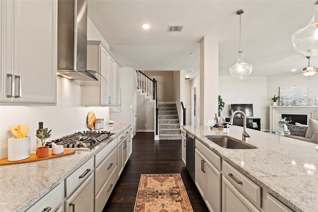 kitchen with dark hardwood / wood-style flooring, stainless steel appliances, sink, wall chimney range hood, and hanging light fixtures