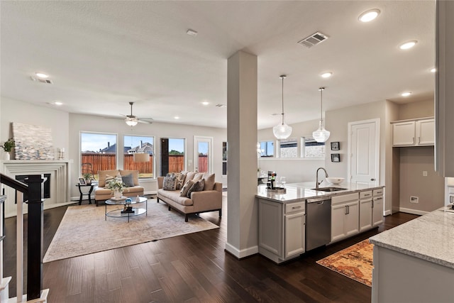 kitchen with light stone counters, dark hardwood / wood-style flooring, stainless steel dishwasher, decorative light fixtures, and white cabinets