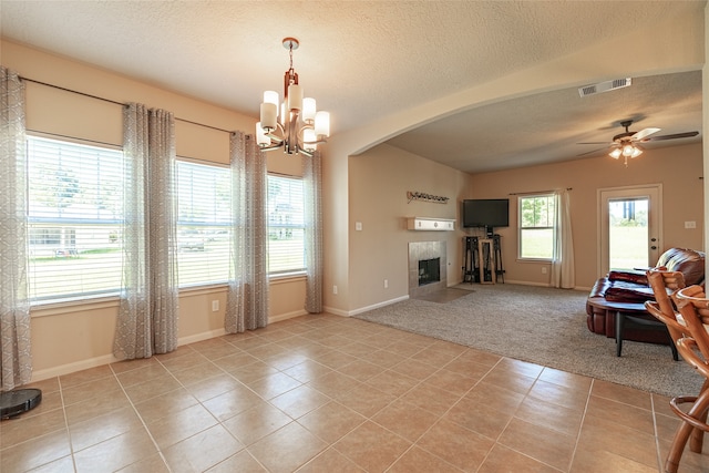 tiled living room with a textured ceiling, a tiled fireplace, and ceiling fan with notable chandelier