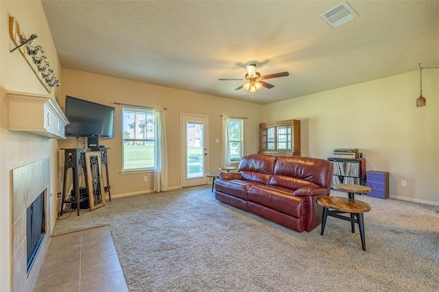 carpeted living room with ceiling fan, a fireplace, and a textured ceiling