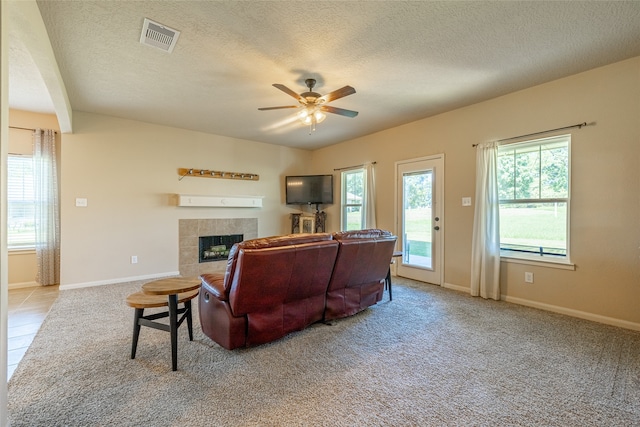 living room with a textured ceiling, a fireplace, light colored carpet, and ceiling fan