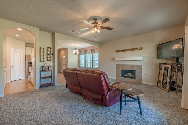 living room with a tile fireplace, a textured ceiling, ceiling fan with notable chandelier, and light colored carpet