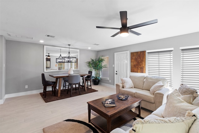 living room with light hardwood / wood-style floors and ceiling fan with notable chandelier