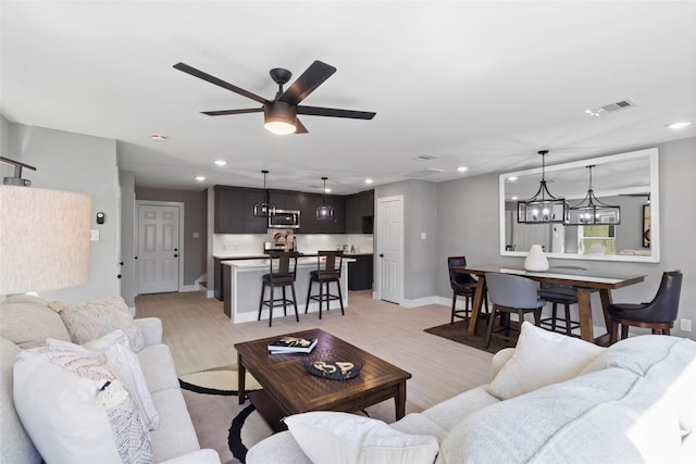 living room with light wood-type flooring and ceiling fan with notable chandelier