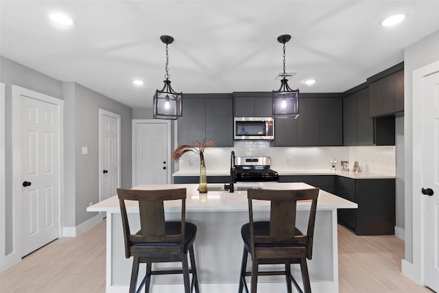 kitchen with light hardwood / wood-style floors, decorative backsplash, pendant lighting, and appliances with stainless steel finishes