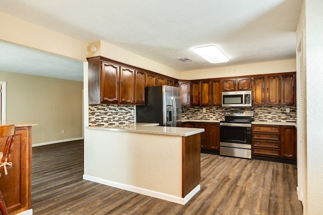 kitchen featuring appliances with stainless steel finishes, dark wood-type flooring, backsplash, and kitchen peninsula