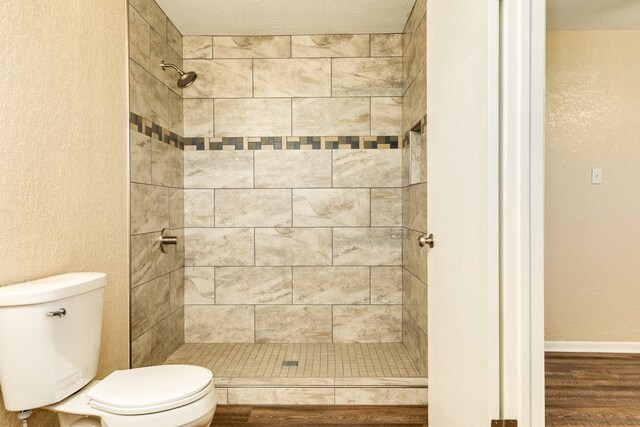 bathroom featuring wood-type flooring, a tile shower, toilet, and a textured ceiling