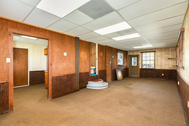 empty room with a paneled ceiling, wooden walls, and carpet flooring