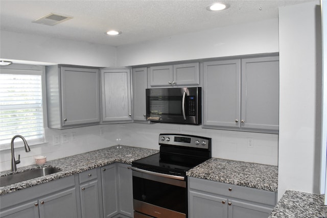 kitchen featuring decorative backsplash, dark stone countertops, gray cabinets, stainless steel appliances, and sink