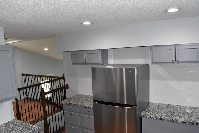 kitchen featuring gray cabinetry, a textured ceiling, dark stone counters, and stainless steel fridge