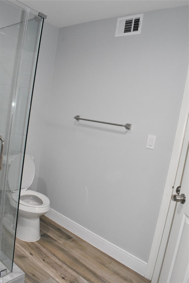 bathroom with hardwood / wood-style floors, walk in shower, and toilet