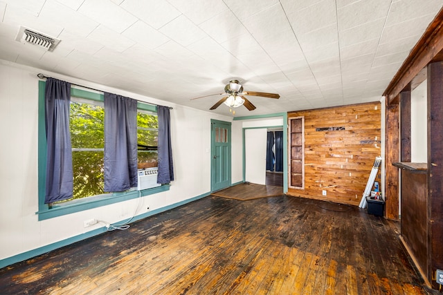 empty room featuring ceiling fan, cooling unit, dark wood-type flooring, and wooden walls