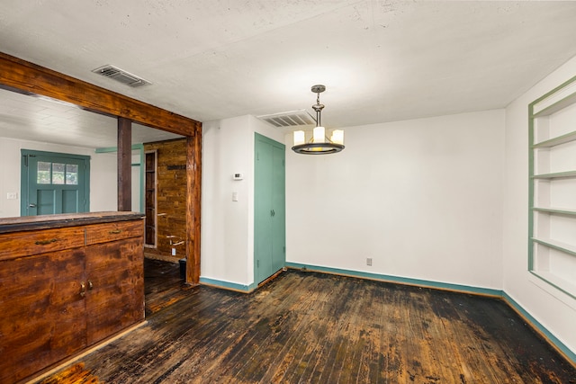 empty room with built in shelves, dark wood-type flooring, and a chandelier