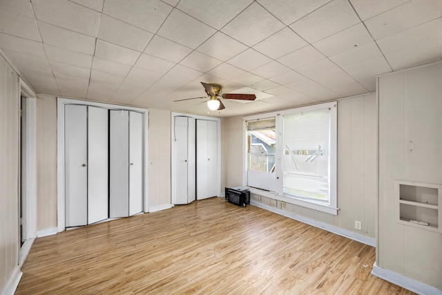 unfurnished bedroom featuring ceiling fan, light hardwood / wood-style floors, and multiple closets