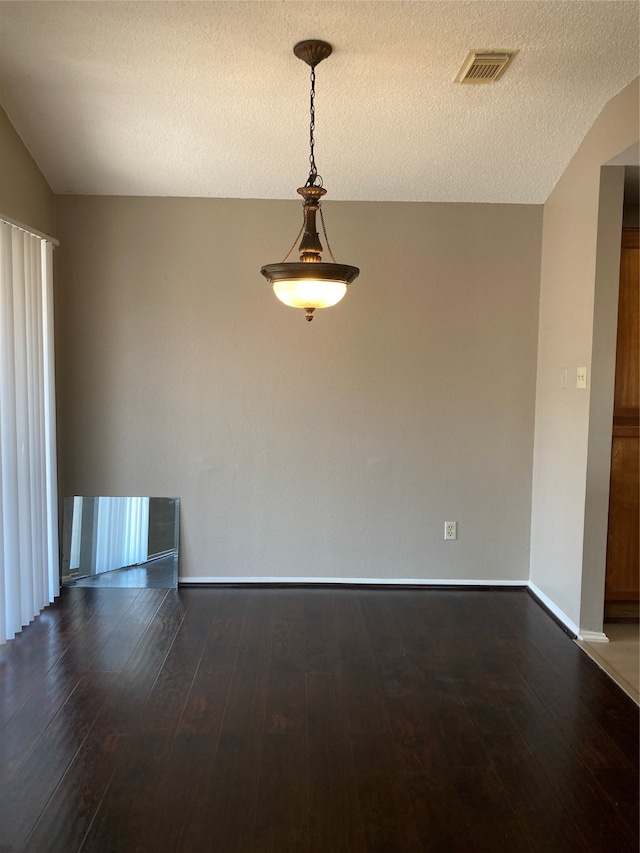 empty room with a textured ceiling, dark hardwood / wood-style floors, and vaulted ceiling