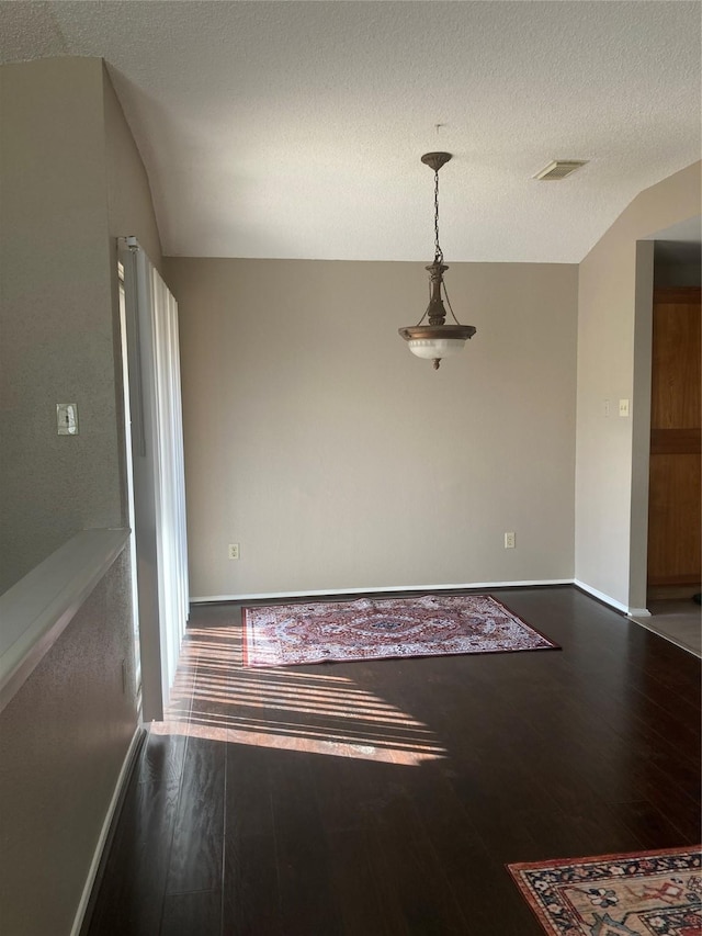 empty room featuring a textured ceiling, vaulted ceiling, and hardwood / wood-style flooring