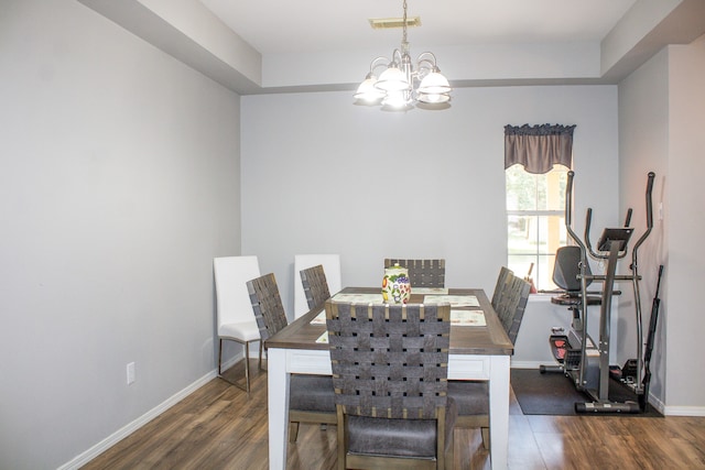 dining area with a notable chandelier, dark hardwood / wood-style floors, and a raised ceiling