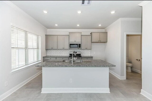 kitchen featuring decorative backsplash, stone countertops, a kitchen island with sink, and light tile patterned floors