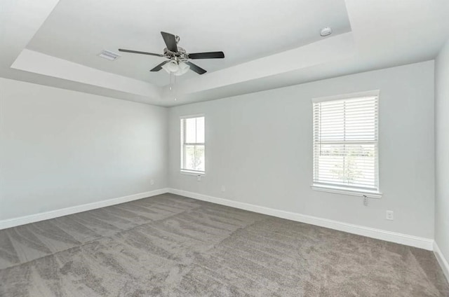 carpeted spare room featuring ceiling fan, a raised ceiling, and a healthy amount of sunlight