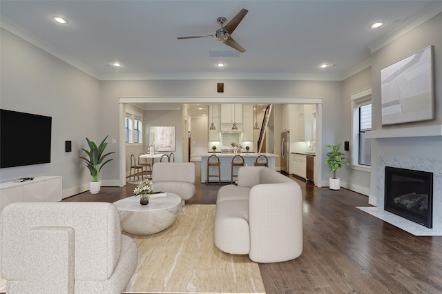 living room with ceiling fan, wood-type flooring, a high end fireplace, and ornamental molding