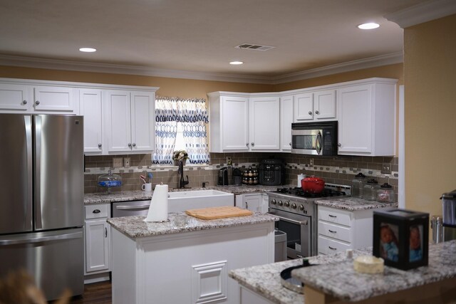 kitchen featuring white cabinets, stainless steel appliances, a center island, and light stone countertops