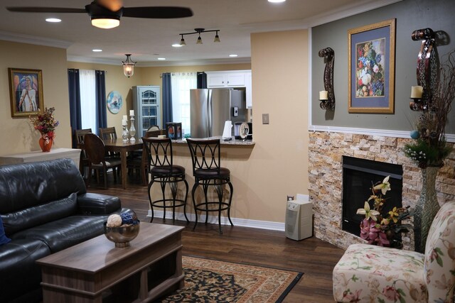 living room featuring dark wood-style flooring, crown molding, recessed lighting, a stone fireplace, and baseboards