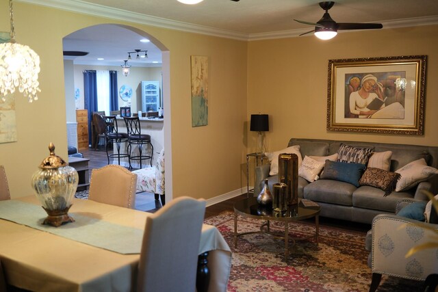 living area with arched walkways, crown molding, a ceiling fan, wood finished floors, and baseboards