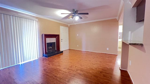 unfurnished living room featuring ceiling fan, crown molding, hardwood / wood-style flooring, a healthy amount of sunlight, and a tiled fireplace