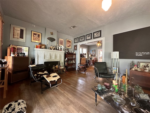 living room featuring ceiling fan, a textured ceiling, hardwood / wood-style floors, and a fireplace