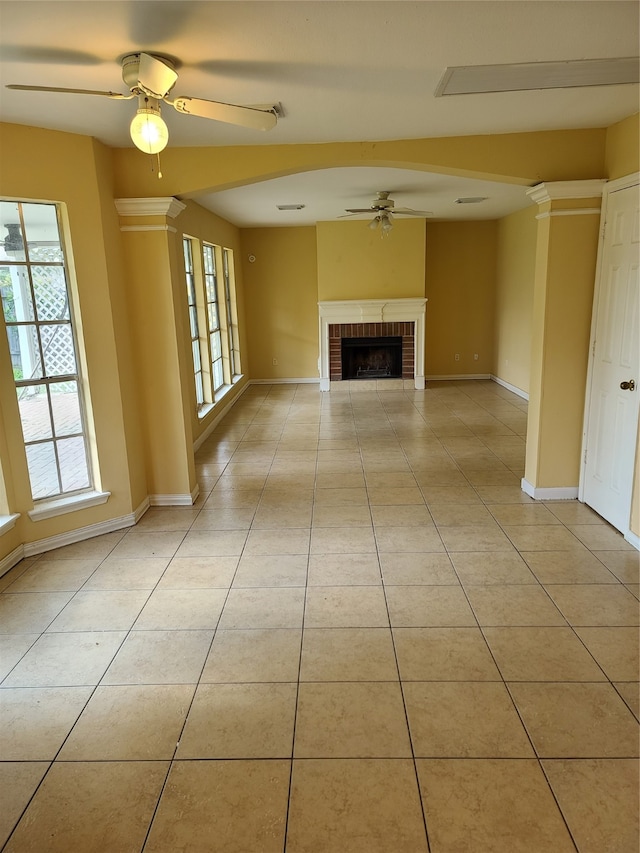 unfurnished living room featuring ceiling fan, ornate columns, a brick fireplace, and light tile patterned floors