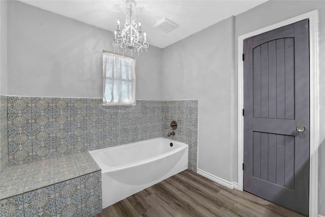 bathroom featuring tile walls, a chandelier, a bathtub, and hardwood / wood-style floors