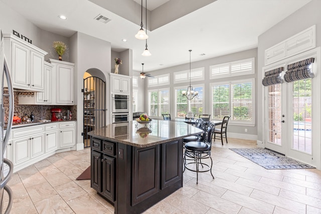 kitchen featuring appliances with stainless steel finishes, tasteful backsplash, dark stone counters, ceiling fan with notable chandelier, and a kitchen island