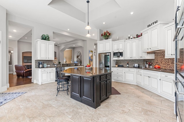 kitchen featuring decorative backsplash, appliances with stainless steel finishes, a kitchen island, and dark stone counters