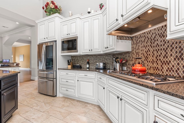 kitchen featuring white cabinetry, stainless steel appliances, crown molding, dark stone counters, and custom range hood