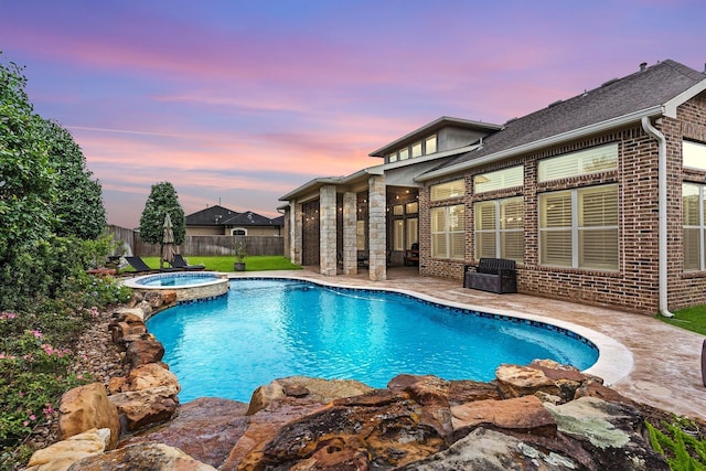 pool at dusk with an in ground hot tub and a patio