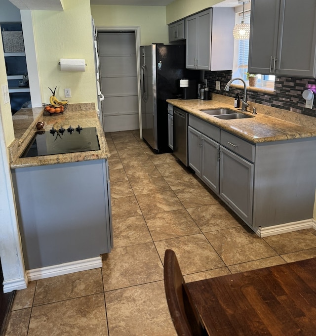 kitchen with tasteful backsplash, pendant lighting, dishwasher, sink, and black electric stovetop