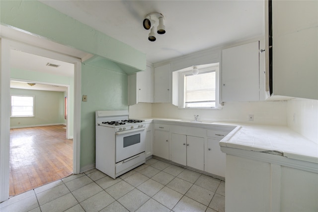 kitchen featuring sink, light tile patterned floors, white range with gas cooktop, and white cabinetry