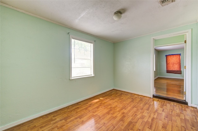 unfurnished room with a textured ceiling, light wood-type flooring, and ornamental molding