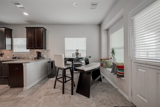 kitchen featuring light stone counters, dark brown cabinetry, and tasteful backsplash