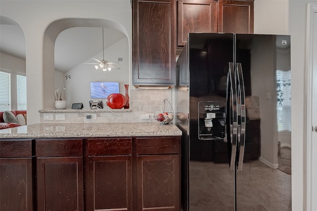 kitchen featuring black fridge, lofted ceiling, kitchen peninsula, backsplash, and light stone countertops