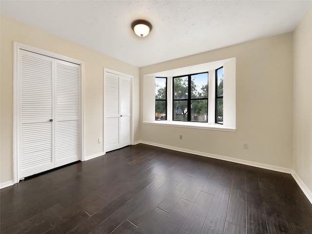 unfurnished bedroom featuring multiple closets and dark wood-type flooring