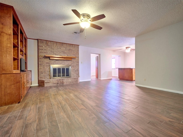 unfurnished living room featuring ceiling fan, a brick fireplace, hardwood / wood-style floors, and a textured ceiling