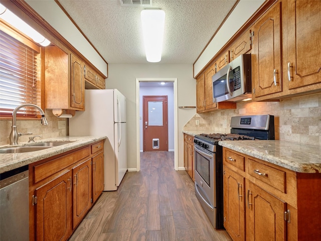 kitchen with sink, decorative backsplash, stainless steel appliances, light stone countertops, and dark wood-type flooring