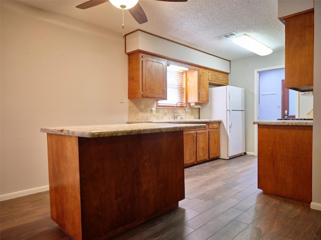 kitchen with sink, white refrigerator, dark hardwood / wood-style floors, kitchen peninsula, and decorative backsplash