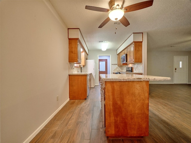 kitchen with dark wood-type flooring, tasteful backsplash, a textured ceiling, kitchen peninsula, and stainless steel appliances